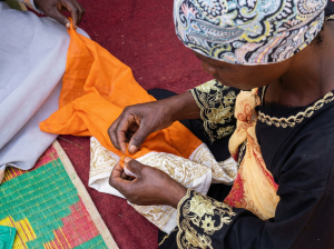 Hands of a woman teaching a youth practical tailoring skills during Fecane's entrepreneurial workshop in Bwaise.
