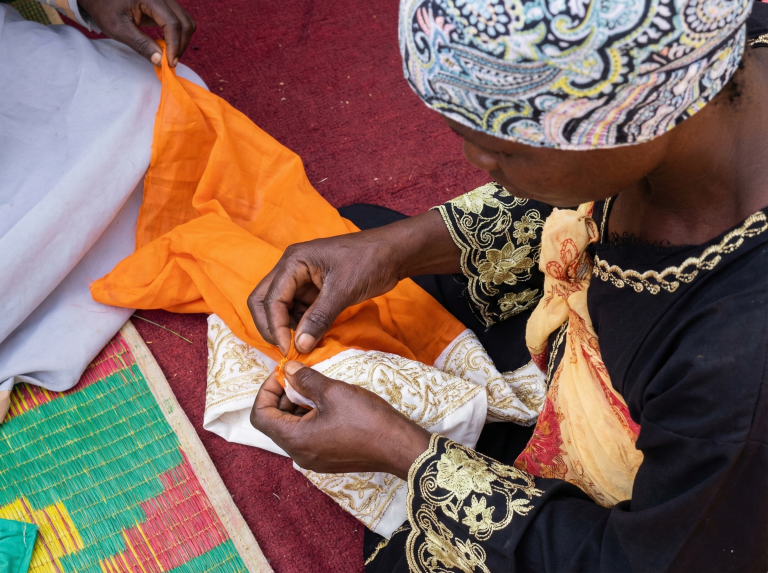 Hands of a woman teaching a youth practical tailoring skills during Fecane's entrepreneurial workshop in Bwaise.